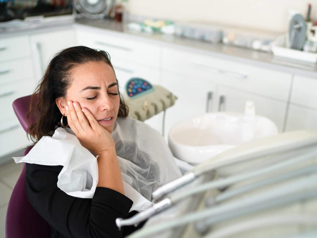 picture of woman in dental chair holding her cheek in pain