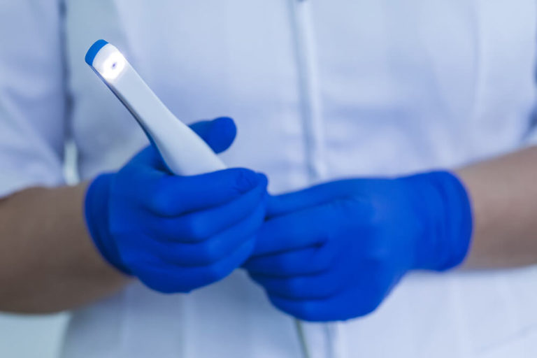 A dental assistant wearing blue medical gloves holds an intraoral camera